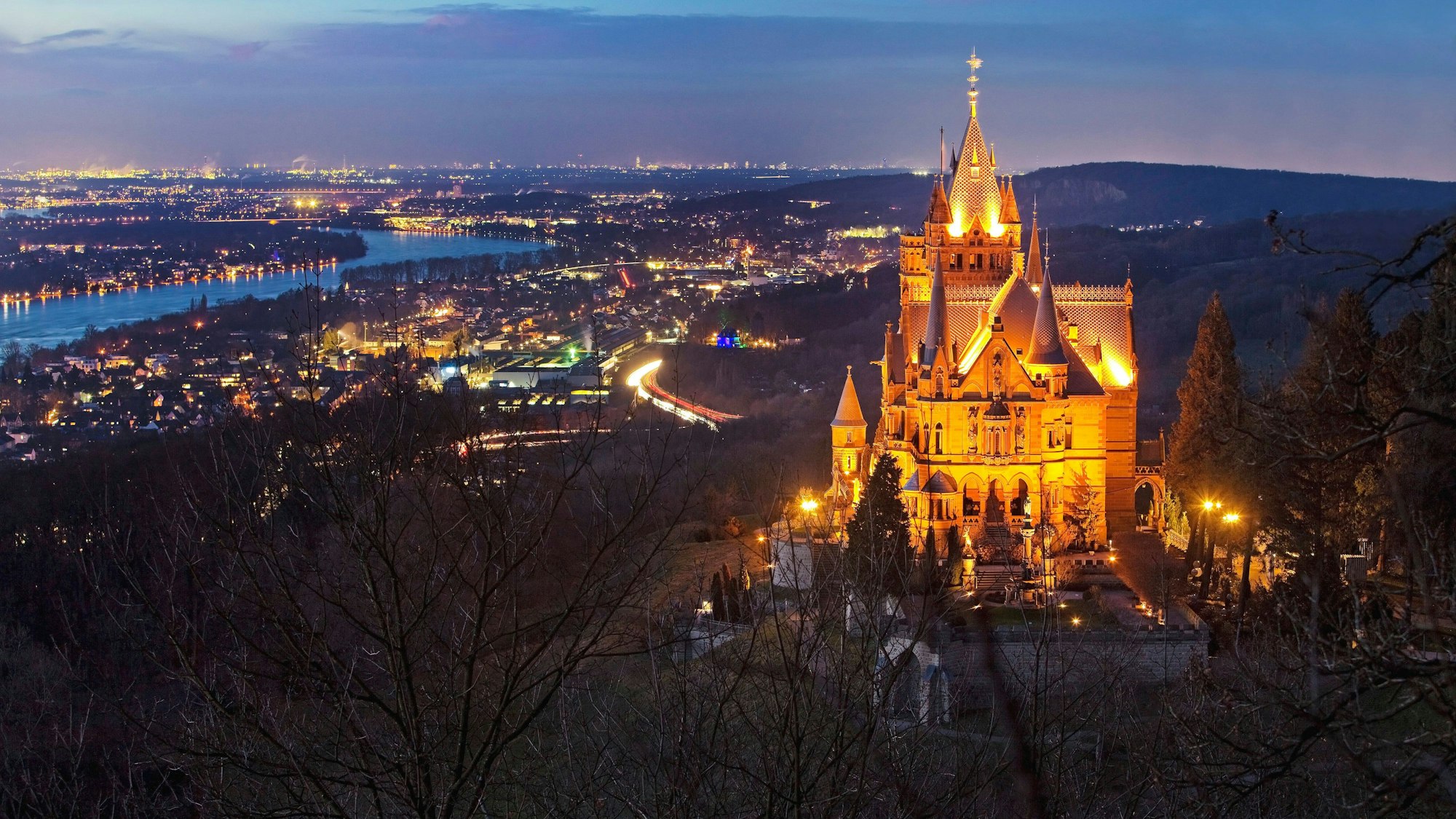 Beleuchtetes Schloss Drachenburg über dem Rheintal am Abend.