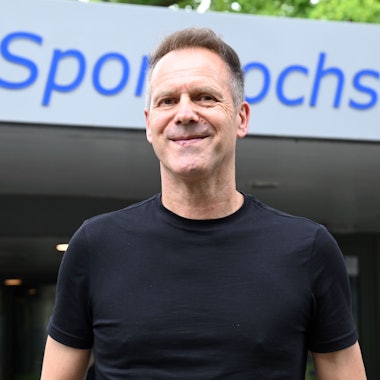 Ansgar Thiel vor dem Eingang am Hauptgebäude, mit dem Schriftzug Deutsche Sporthochschule Köln.