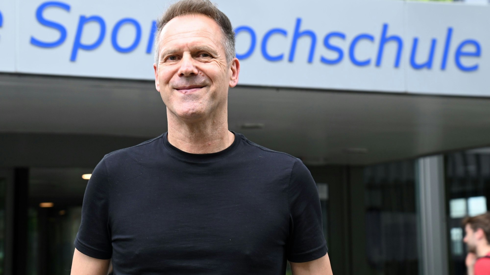 Ansgar Thiel vor dem Eingang am Hauptgebäude, mit dem Schriftzug Deutsche Sporthochschule Köln.