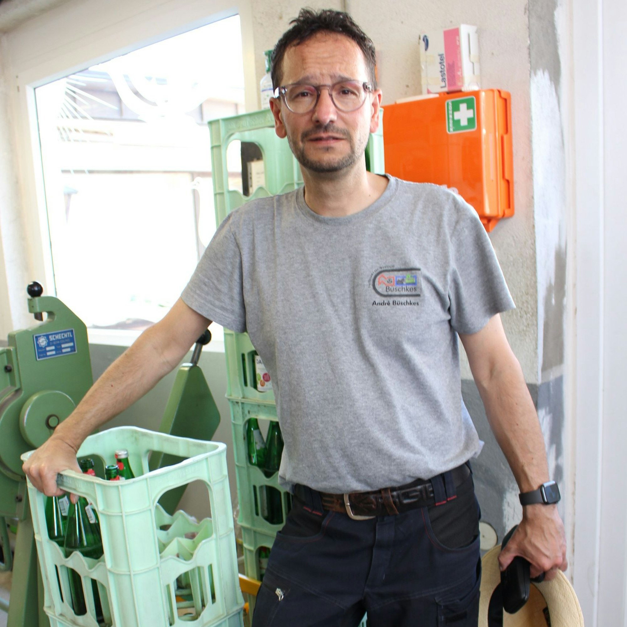 Ein lehnt in grauem Poloshirt und dunkler Arbeitshose gegen mehrere hellgrüne Wasserkästen.