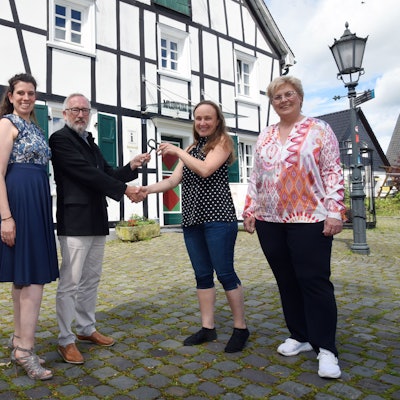 Gruppenfoto dreier Frauen und eines Mannes vor dem Heimatmuseum in Bergneustadt. Symbolisch wird ein großer Schlüssel überreicht.