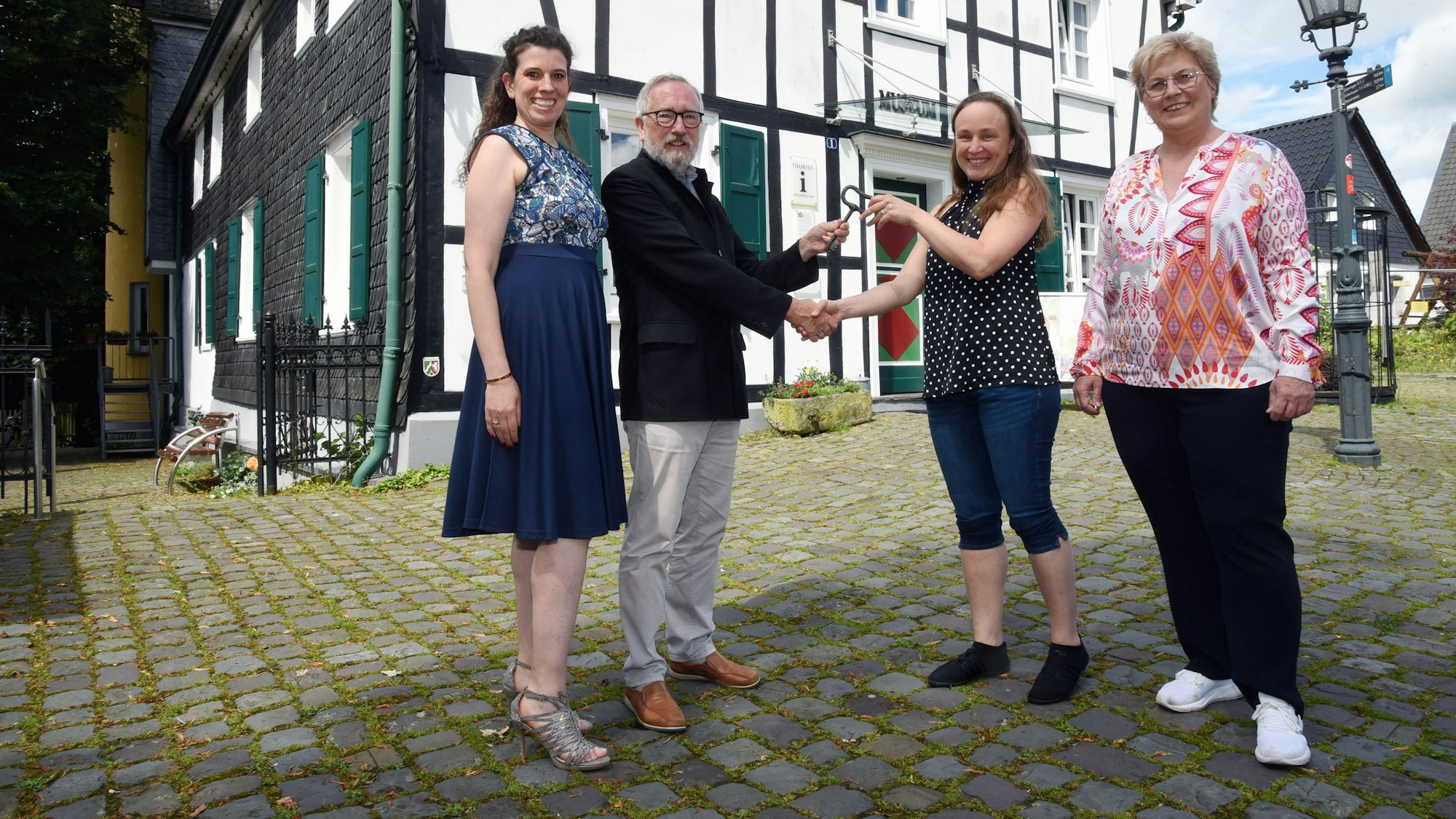 Gruppenfoto dreier Frauen und eines Mannes vor dem Heimatmuseum in Bergneustadt. Symbolisch wird ein großer Schlüssel überreicht.