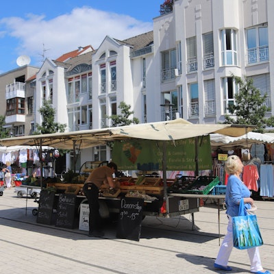 Marktstände mit Obst und Kleidung auf dem Hennefer Marktplatz, eine Frau mit Einkaufstasche geht vorbei.
