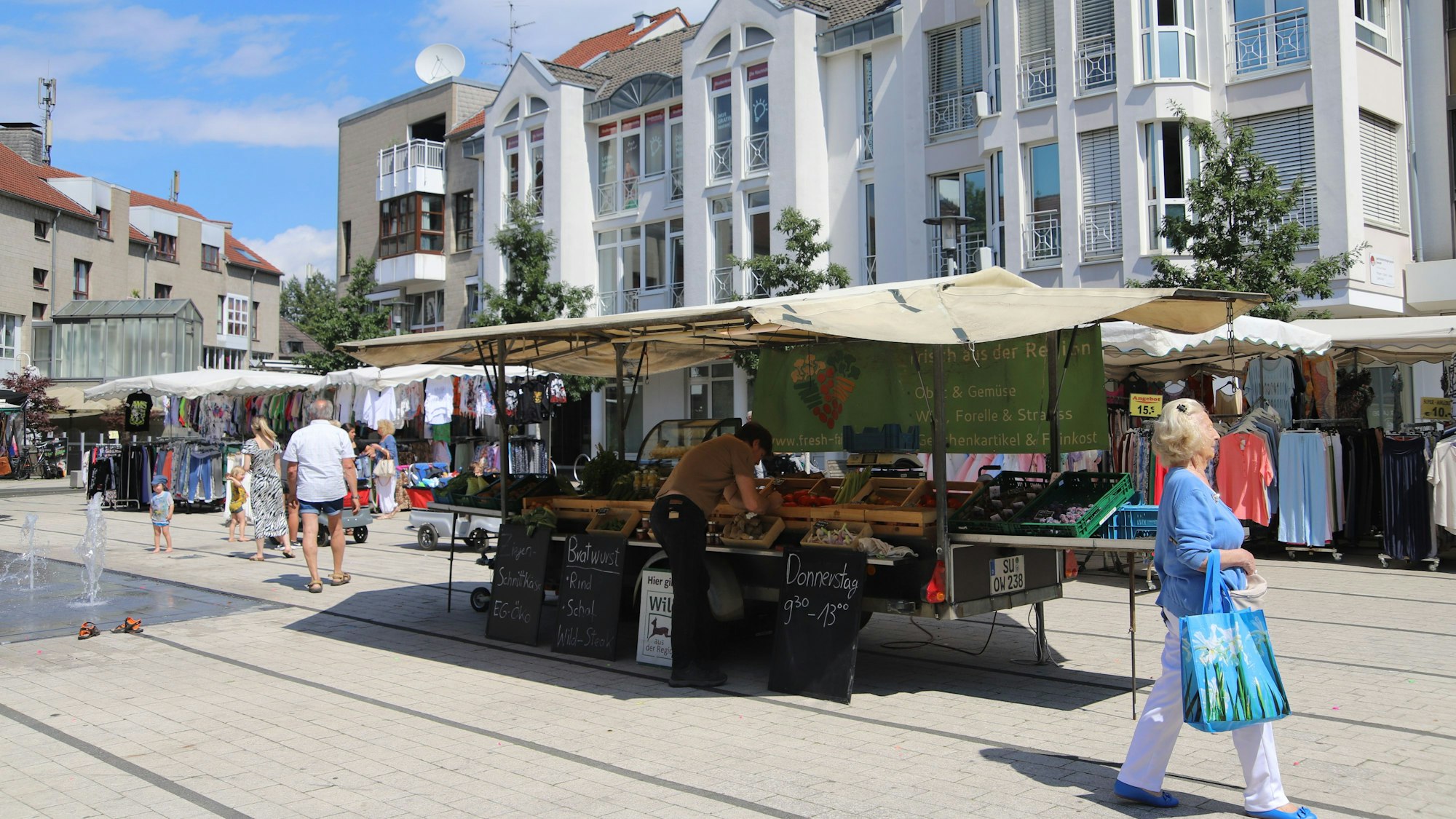 Marktstände mit Obst und Kleidung auf dem Hennefer Marktplatz, eine Frau mit Einkaufstasche geht vorbei.