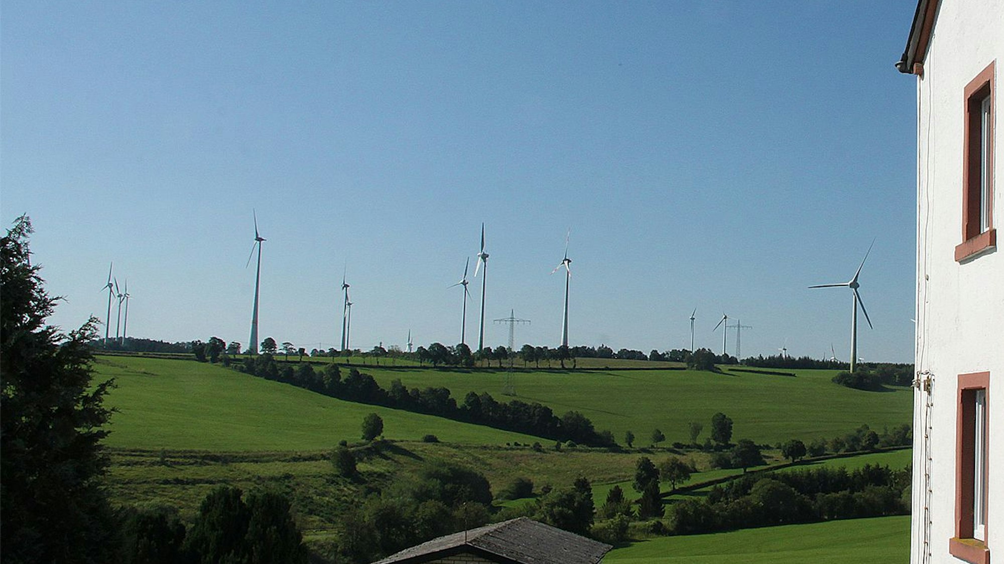Mehrere Windräder stehen vor blauen Himmel am Horizont auf einem grünen Hügel.