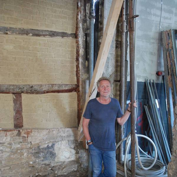 Josef Mütters steht inmitten einer Baustelle. Er hält sich an einem Rohr fest. Im Hintergrund ist eine nackte Steinwand zu sehen.