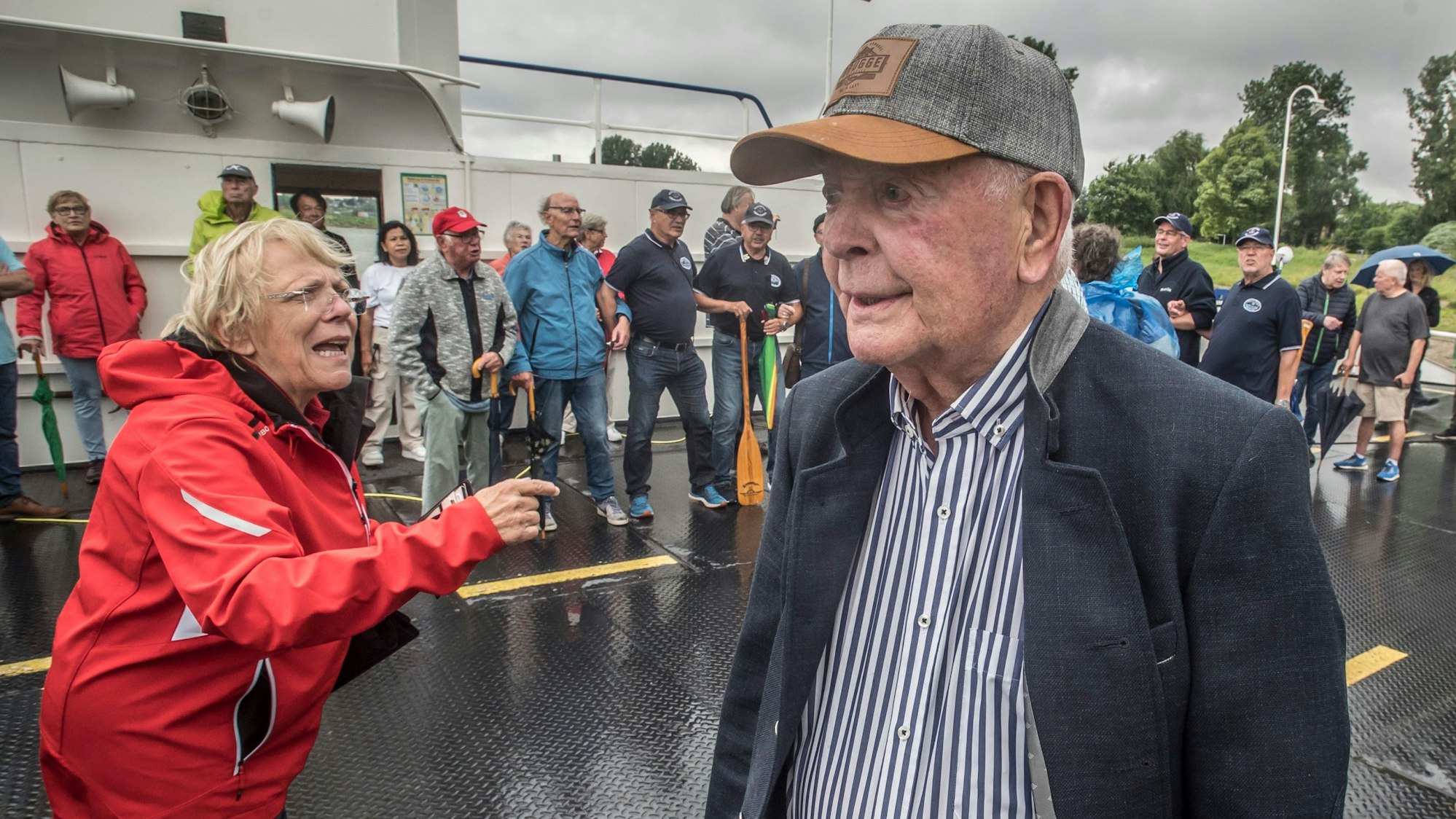 Ein Mann mit einer Schirmkappe steht auf einem Schiff mit vielen anderen Menschen.