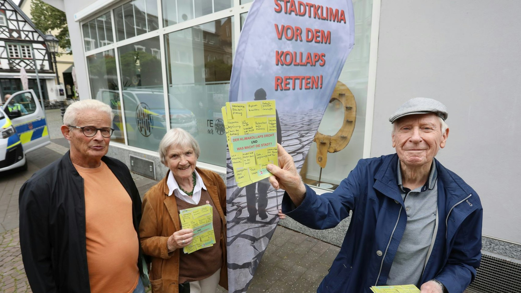 Zwei Männer und eine Frau stehen vor einem Aufsteller mit der Aufschrift „Stadtklima vor dem Kollaps retten" und zeigen Flugblätter.