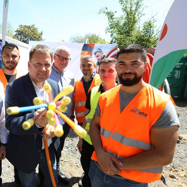 Eine Gruppe von Männern, zum Teil mit Warnwesten gekleidet, halten ein Glasfaserkabel in die Kamera.