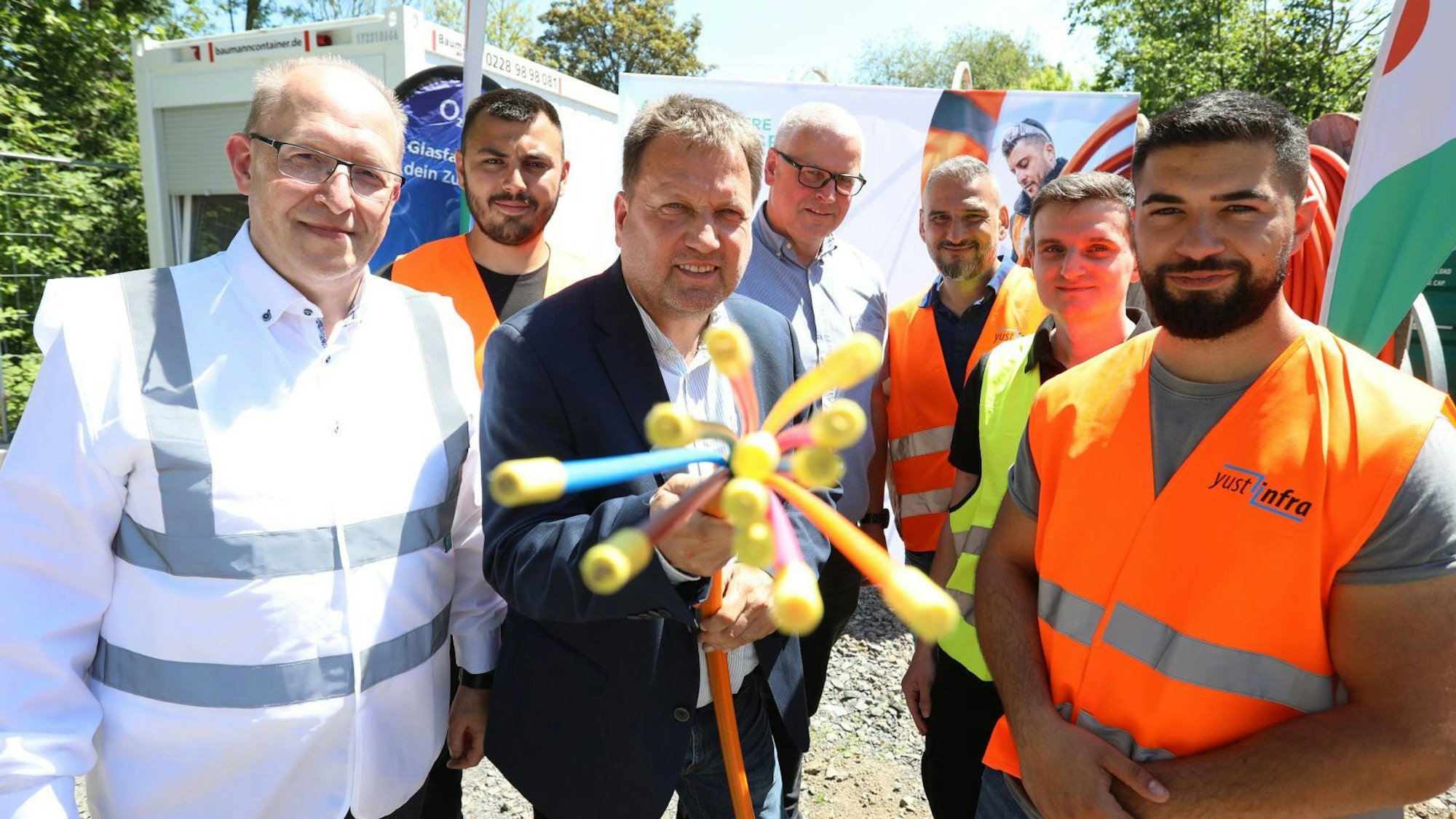 Eine Gruppe von Männern, zum Teil mit Warnwesten gekleidet, halten ein Glasfaserkabel in die Kamera.