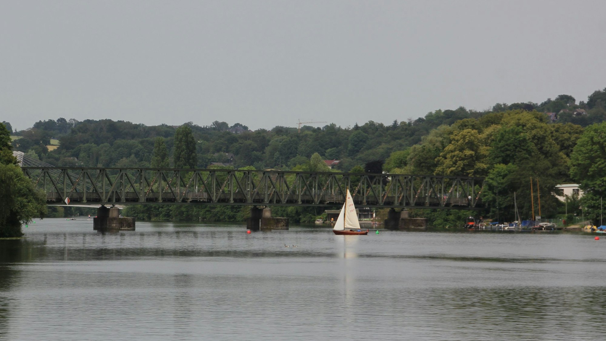 Vor einer Fachwerkbrücke kreuzt ein Segelboot auf dem Baldeneysee in Essen.