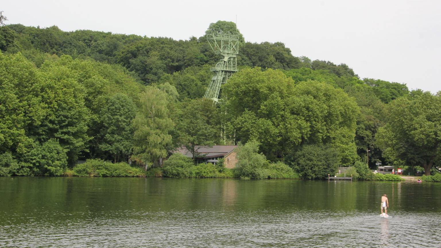 Inmitten von Bäumen steht ein stillgelegter Förderturm am Ufer des Essener Baldeneysess.