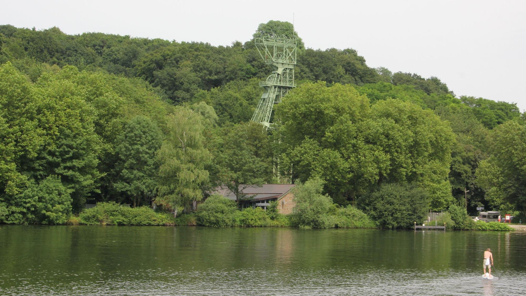 Inmitten von Bäumen steht ein stillgelegter Förderturm am Ufer des Essener Baldeneysess.
