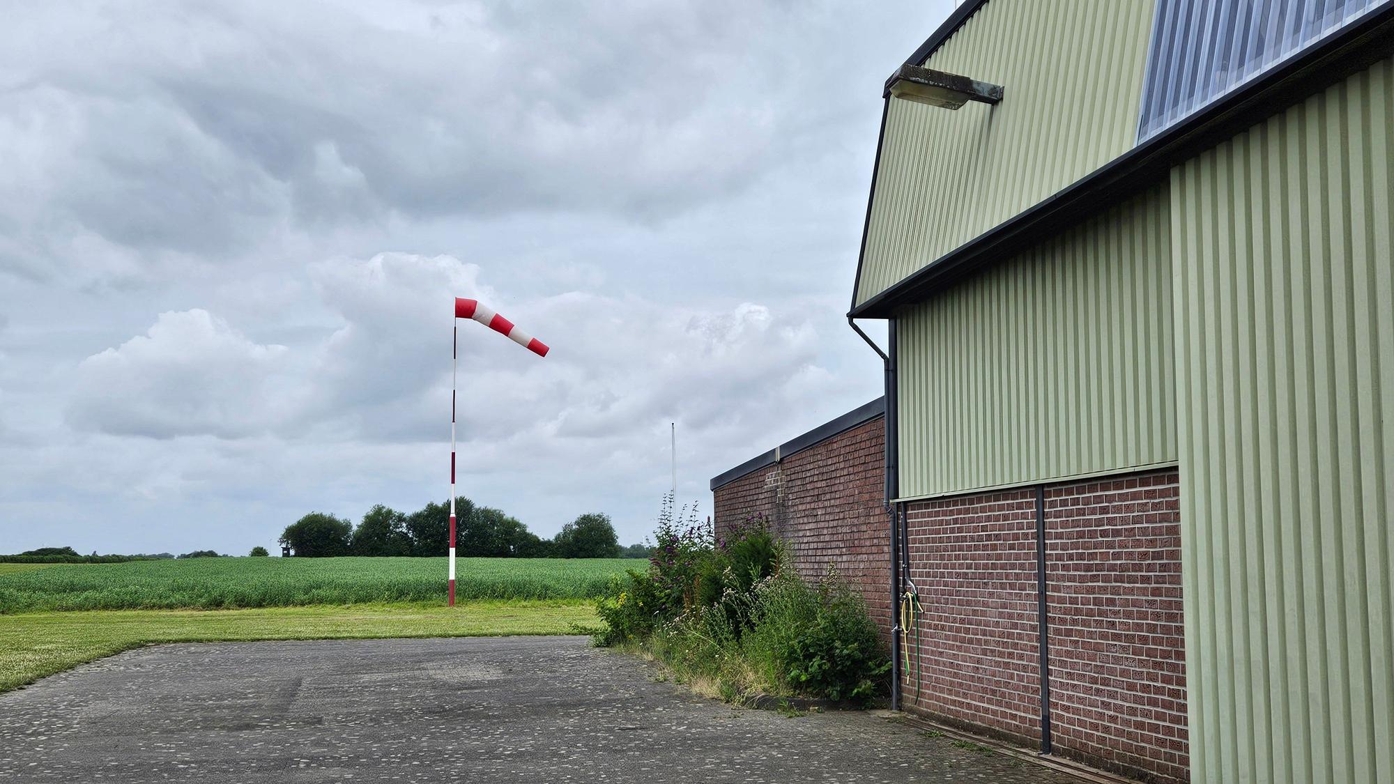 Zu sehen ist eine Halle, neben der ein Windsack steht.
