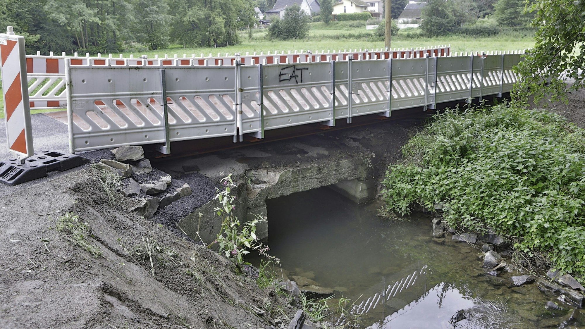 Warnbaken säumen die Fahrbahn auf einer Brücke über einen kleinen Bach.