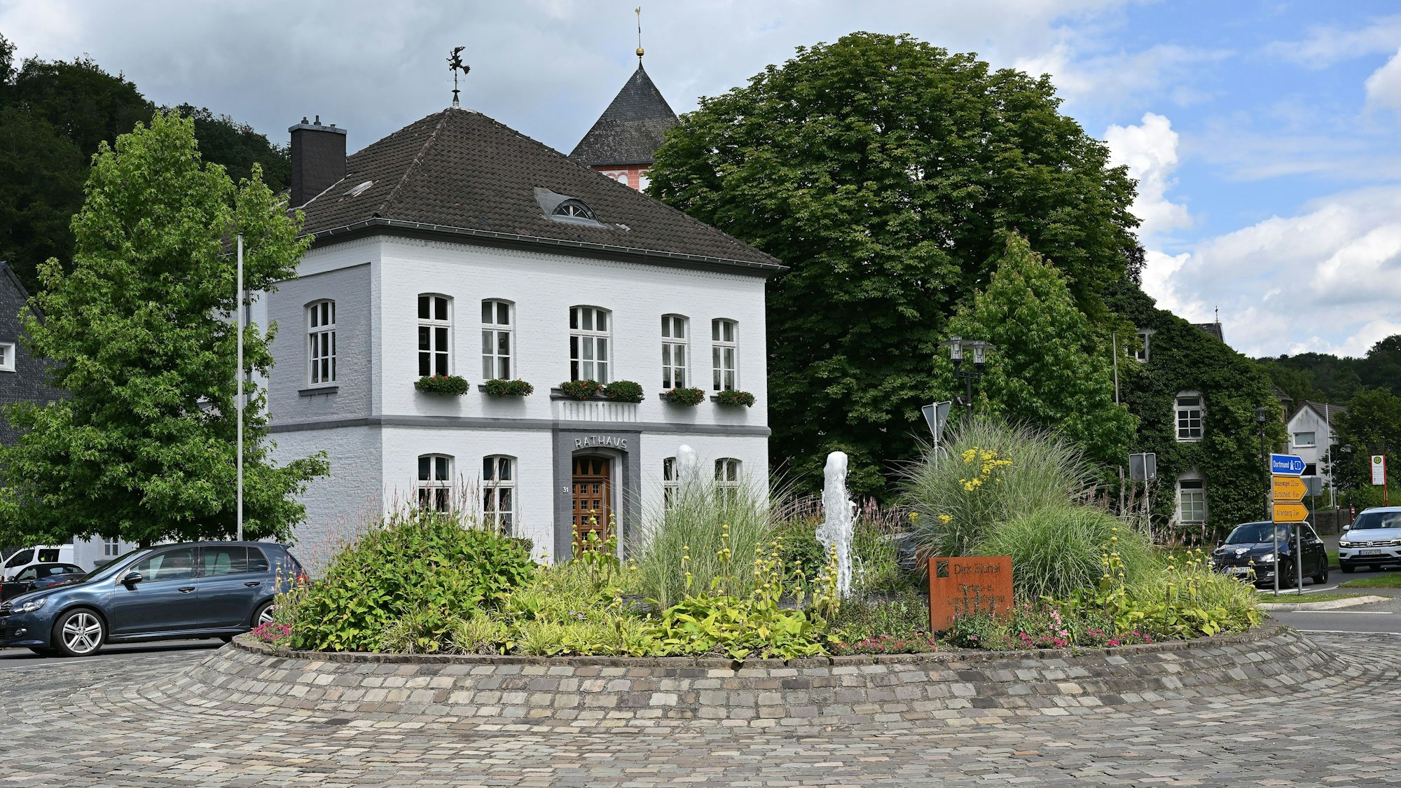 Der Kreisverkehr in Odenthal mit Springbrunnen und Blumen, dahinter das Rathaus.