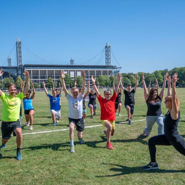 Menschen trainieren gemeinsam auf den Kölner Jahnwiesen. Im Hintergrund ist das Rhein-Energie-Stadion zu sehen.