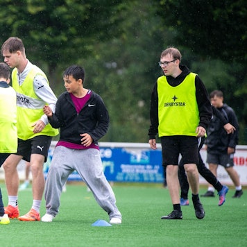 Das Bild zeigt eine Gruppe von Jugendlichen, die auf dem Kunstrasen in Weilerswist im Regen Fußball spielen.