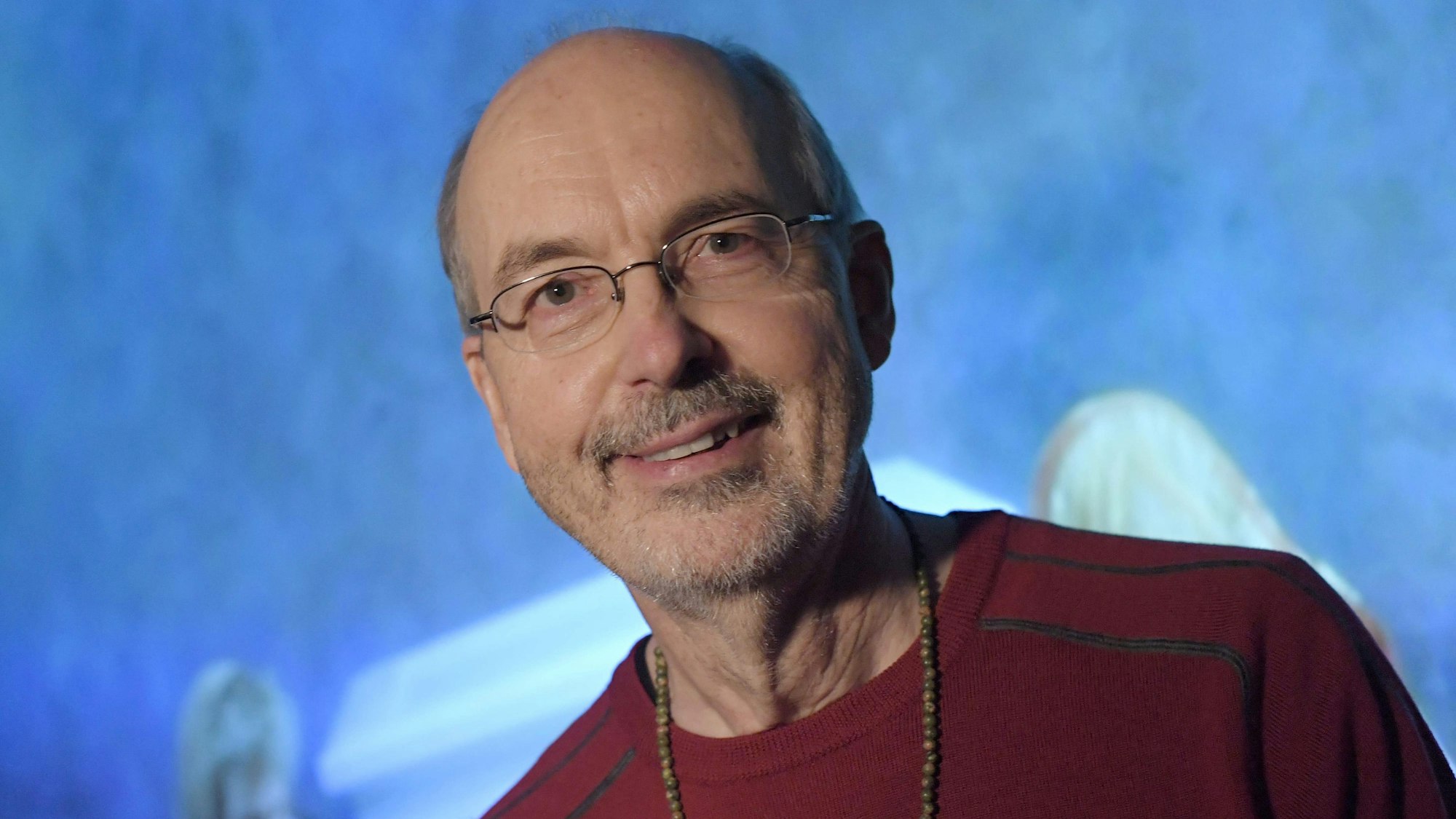 Bill Viola schaut in die Kamera. Er trägt eine Brille, eine Kette und einen roten Pullover.