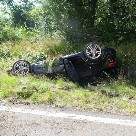 Ein Auto liegt am Straßenrand auf dem Dach.
