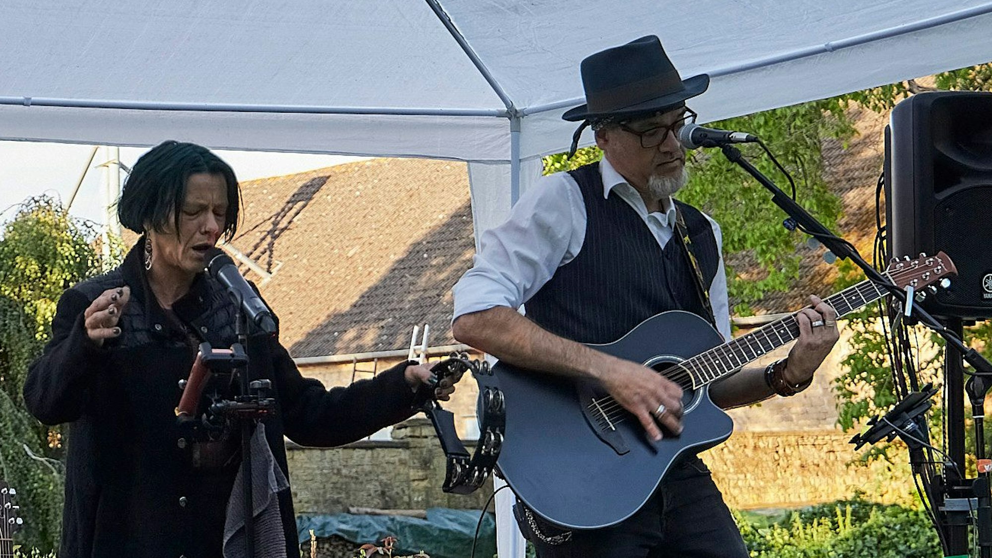 Eine Sängerin und ein Gitarrist stehen unter an einem weißen Pavillon an zwei Mikrofonen und machen Musik.