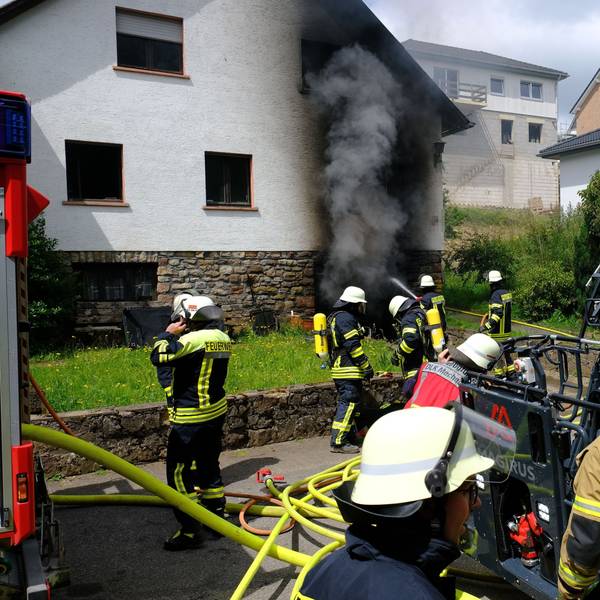 Zahlreiche Feuerwehrleute löschen den Brand in einem Haus in Nettersheim. Aus der Garage im Keller quillt dichter, schwarzer Rauch