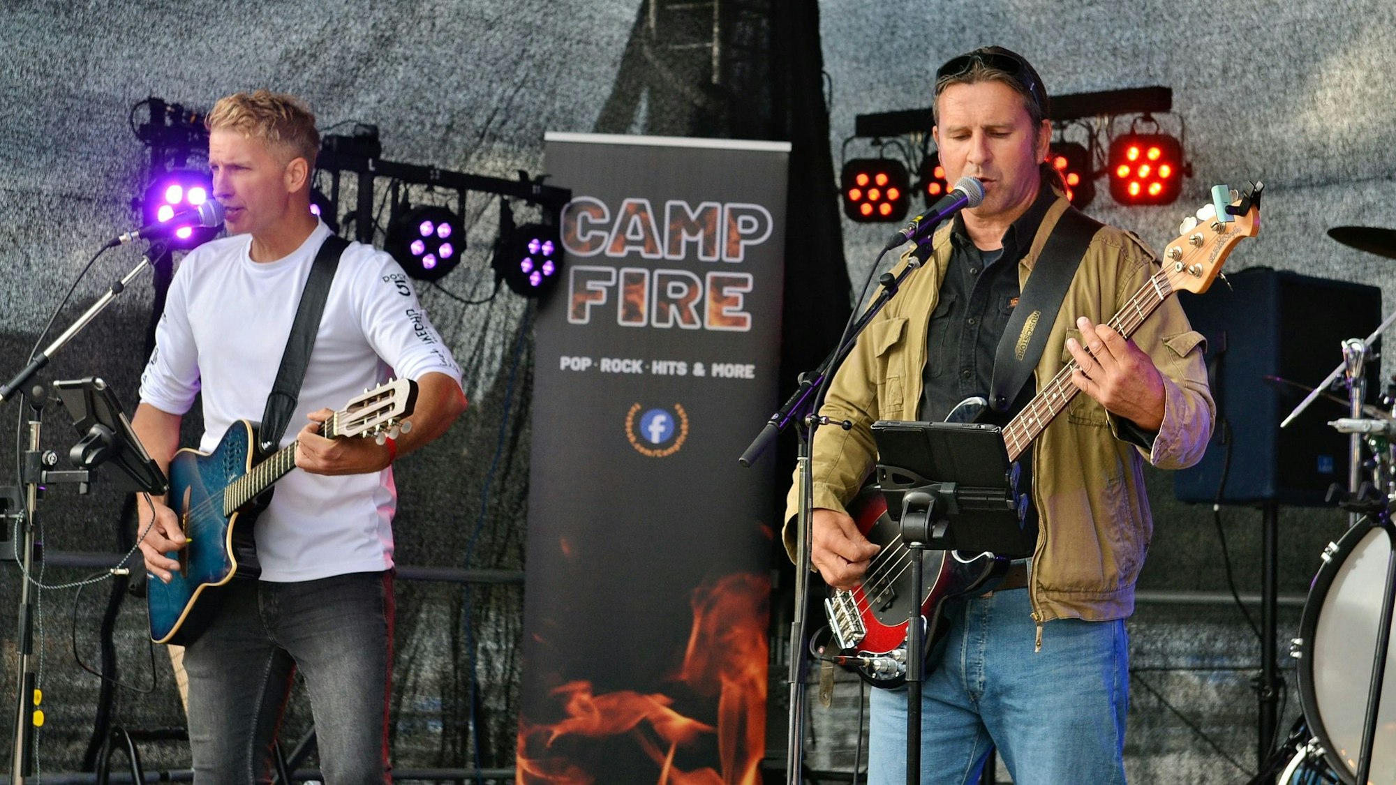 Der Gitarrist und der Bassist der Band Campfire stehen an Mikrofonen auf der Bühne und spielen ihre Instrumente.