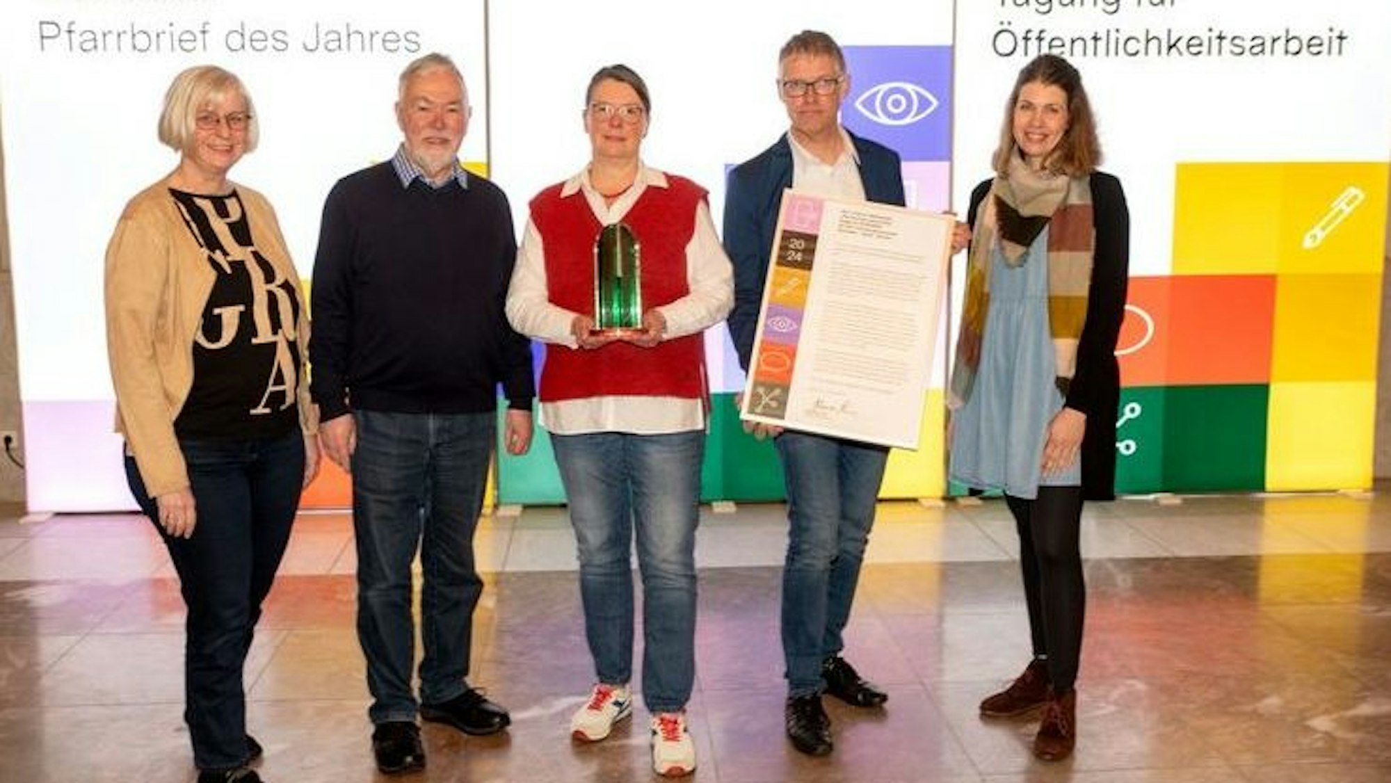 Drei Frauen und zwei Männer lächeln in die Kamera, eine der Frauen hält eine filigrane, grün durchschimmernde Plexiglas-Skulptur in der Hand.