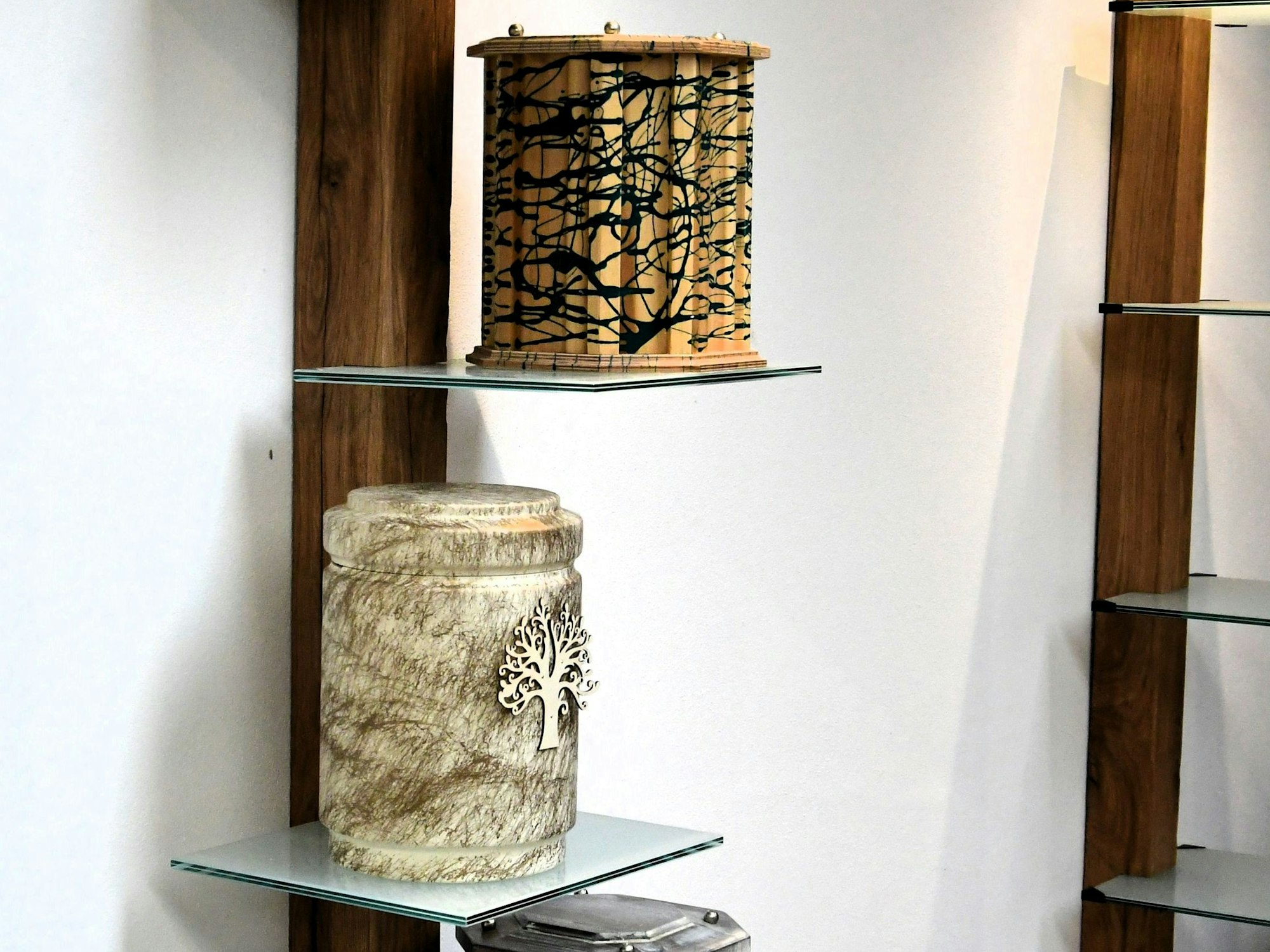 Zwei handgefertigte Urnen aus Holz stehen einzeln auf Regalböden aus Glas.