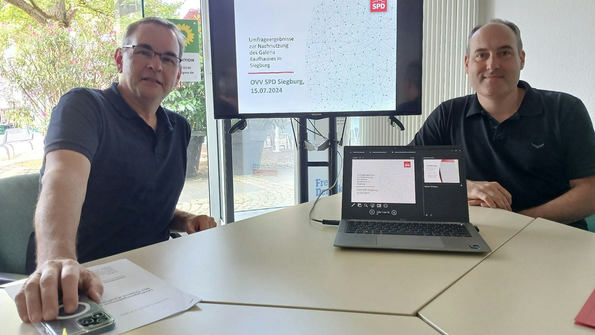 Zwei Männer mit einem Notebook und einer Leinwand im Hintergrund