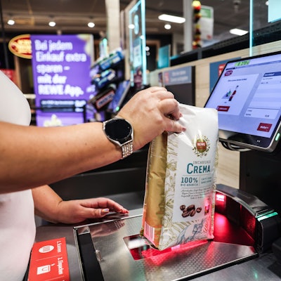 Eine Frau scannt in einer Rewe-Filiale ein Produkt an einer Selbstbedienungskasse.