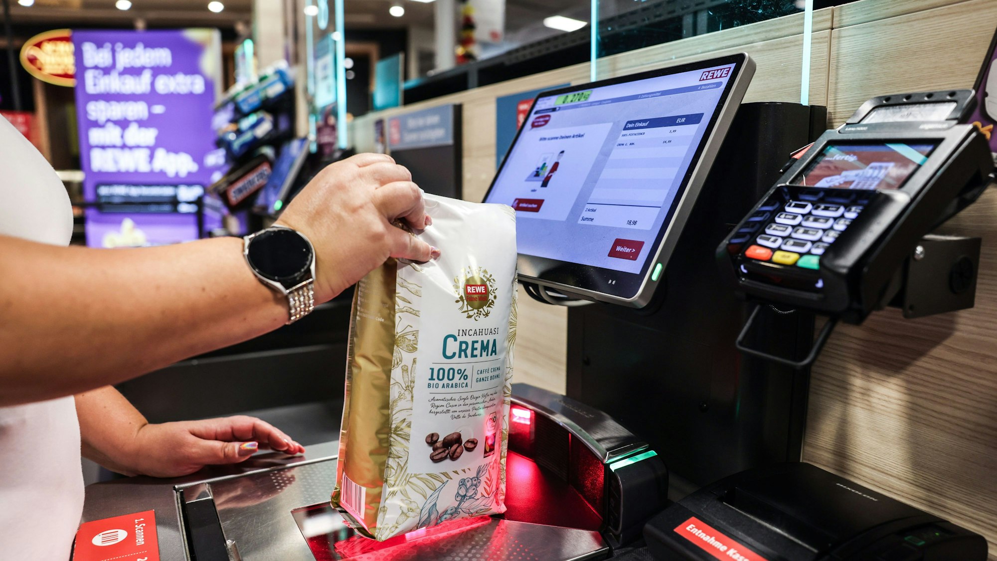 PRODUKTION - 03.07.2024, Nordrhein-Westfalen, Köln: Eine Frau scannt in einer Rewe-Fliale ein Produkt an einer Selbstbedienungskasse. (zu dpa: «Rewe will deutlich mehr Märkte mit SB-Kassen ausstatten») Foto: Oliver Berg/dpa +++ dpa-Bildfunk +++