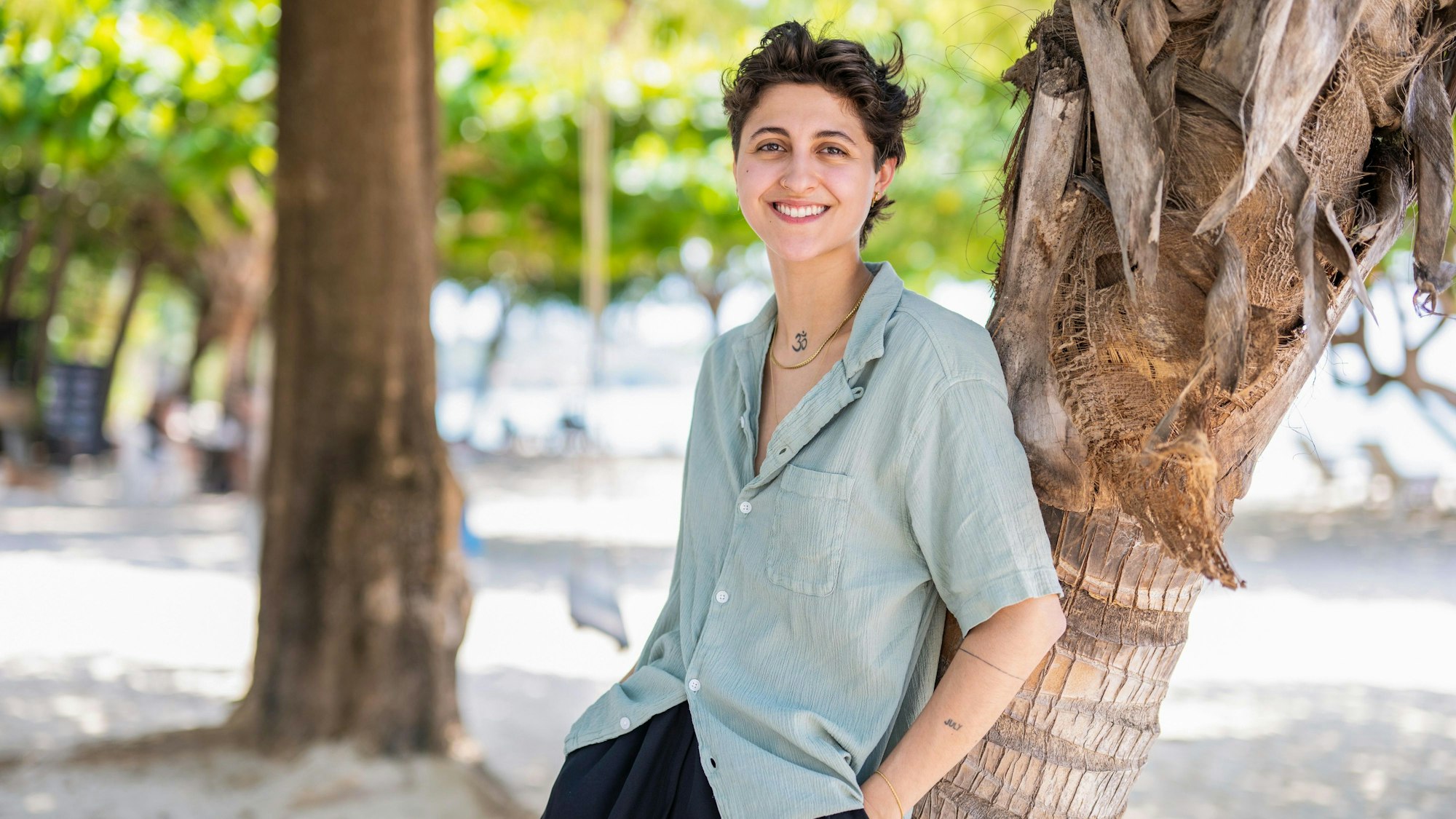 Die Kölnerin Seleya ist Kandidatin der vierten Staffel Princess Charming auf RTL Plus. Auf dem Bild lehnt sie mit dem Rücken an einer Palme und lächelt in Richtung der Kamera.