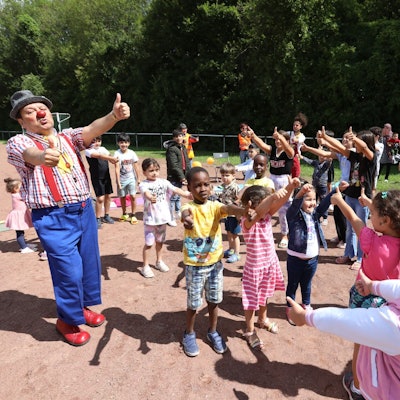 Eine Gruppe von Kindern mit zwei Clowns auf einem Sportplatz.