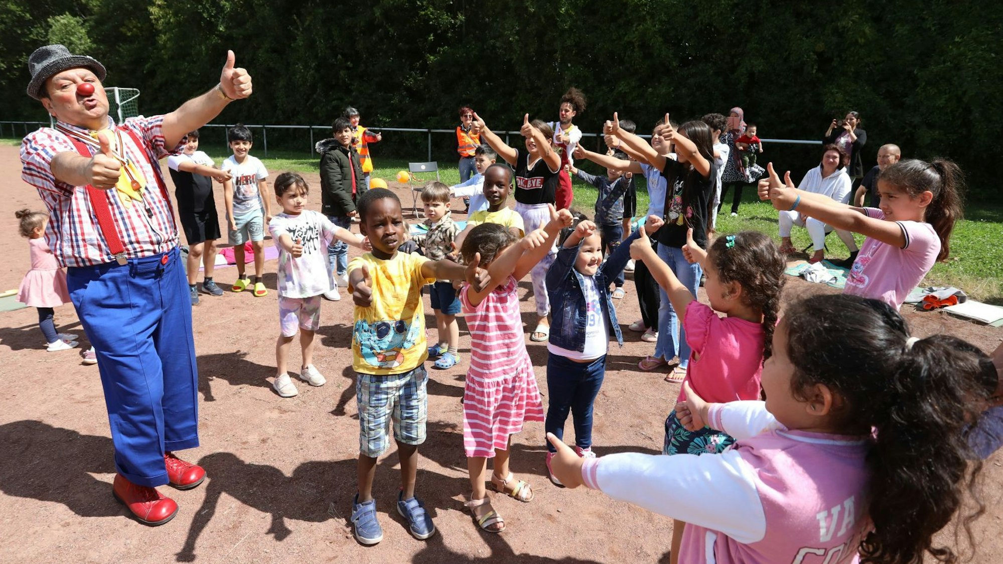 Eine Gruppe von Kindern mit zwei Clowns auf einem Sportplatz.