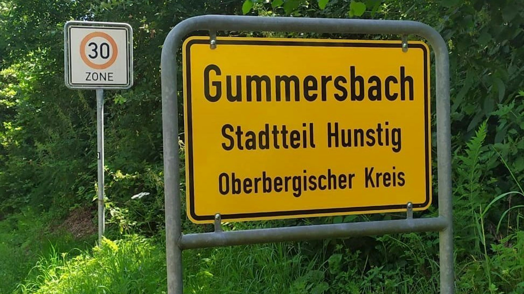 Ein gelbes Ortsschild mit der Aufschrift „Gummersbach, Stadtteil Hunstig, Oberbergischer Kreis“.