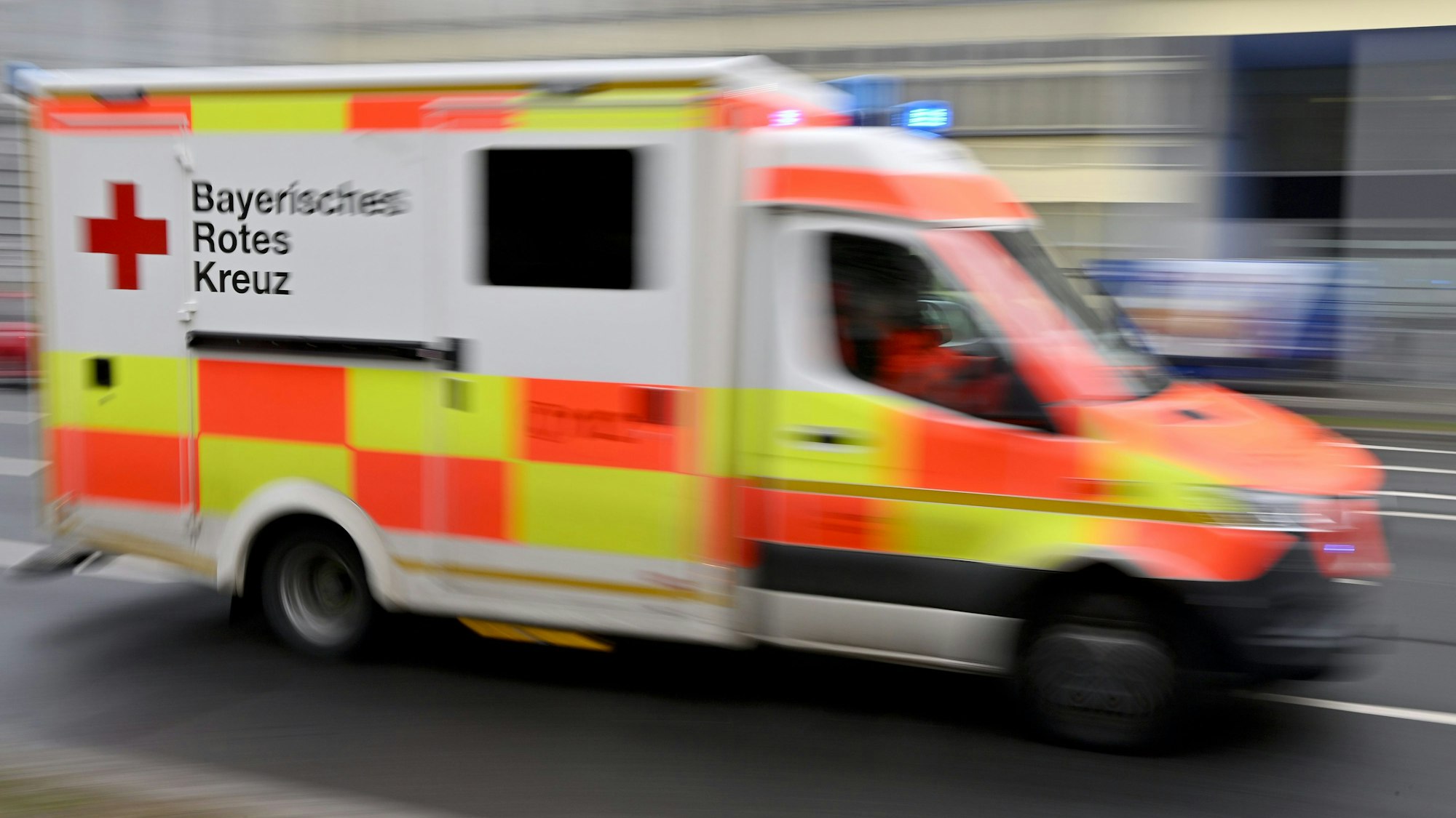 Ein Krankenwagen des Bayerischen Roten Kreuzes (BRK) fährt mit Blaulicht durch die Stadt. (Symboloptik)