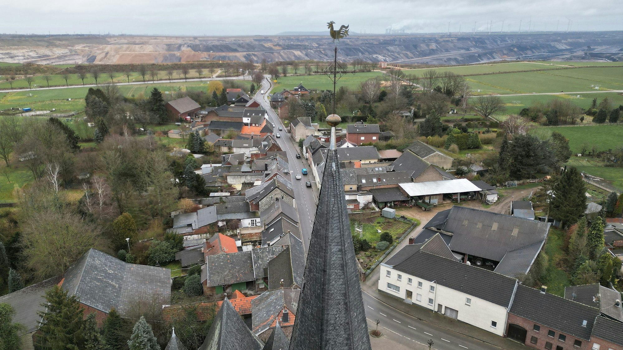 Erkelenz: Die Kirche von Keyenberg steht knapp 500 m von der RWE Braunkohle Tagebau Garzweiler (Aufnahme mit einer Drohne). Durch das auf 2030 vorgezogene Ende der Braunkohleförderung bleiben fünf Dörfer zwischen dem Stadtkern von Erkelenz und dem Tagebau Garzweiler erhalten.
Aus den Dörfern, um die es geht, sind schon 90 Prozent der ursprünglichen Bewohner weggezogen, die meisten Häuser stehen leer. Sie gehören überwiegend dem Energiekonzern RWE. Von den ursprünglich 1500 Bewohnern sind noch 200 verblieben. Hinzu kommen derzeit 300 Geflüchtete aus der Ukraine, die in Häusern leben.