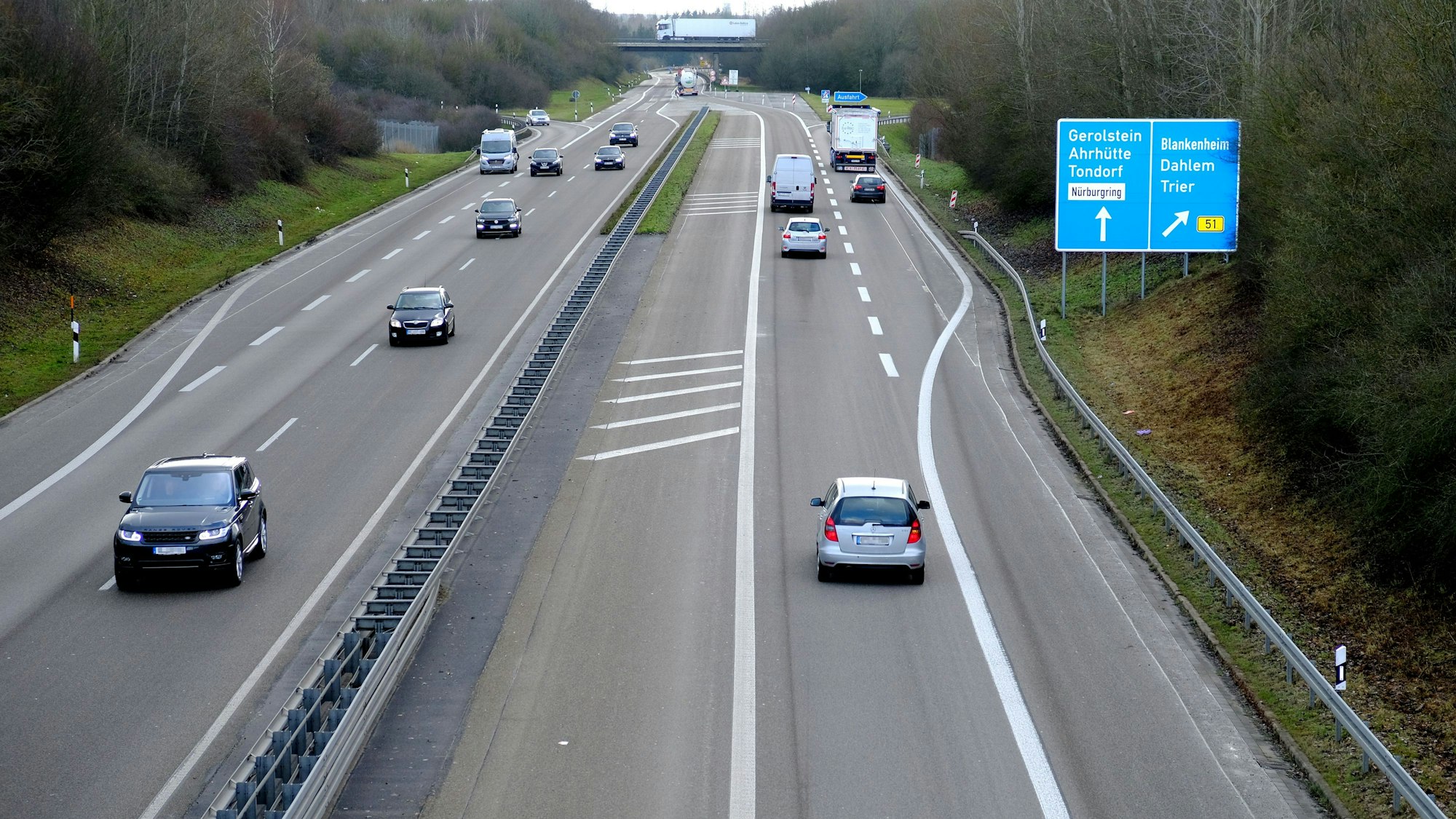Autos fahren auf einer Autobahn. Am Rand stehen Bäume und Sträucher.