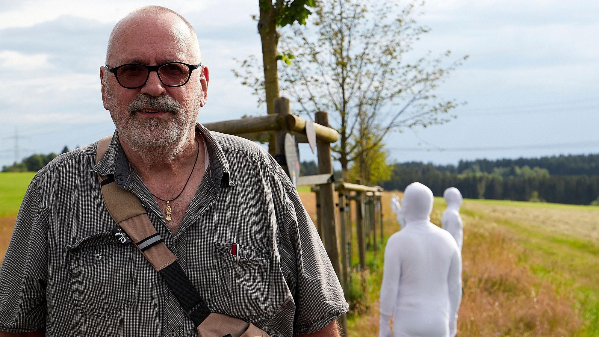 Klaus Jansen aus Odendorf steht an der zentralen Flut-Gedenkstätte des Landes NRW. Hinter ihm sind Teilnehmer einer Kunstaktion in weißen Anzügen zu sehen.