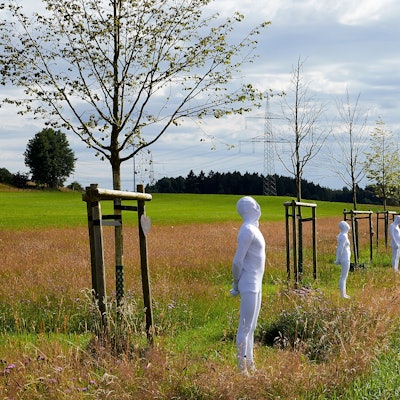 In weiße Anzüge gekleidete Menschen stehen vor den Bäumen der zentralen NRW-Gedenkstätte für die Opfer der Flutkatastrophe. Sie symbolisieren die gestorbenen Menschen.