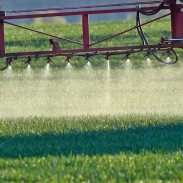 Ein Landwirt fährt mit einer Dünger- und Pestizidspritze über ein Feld.