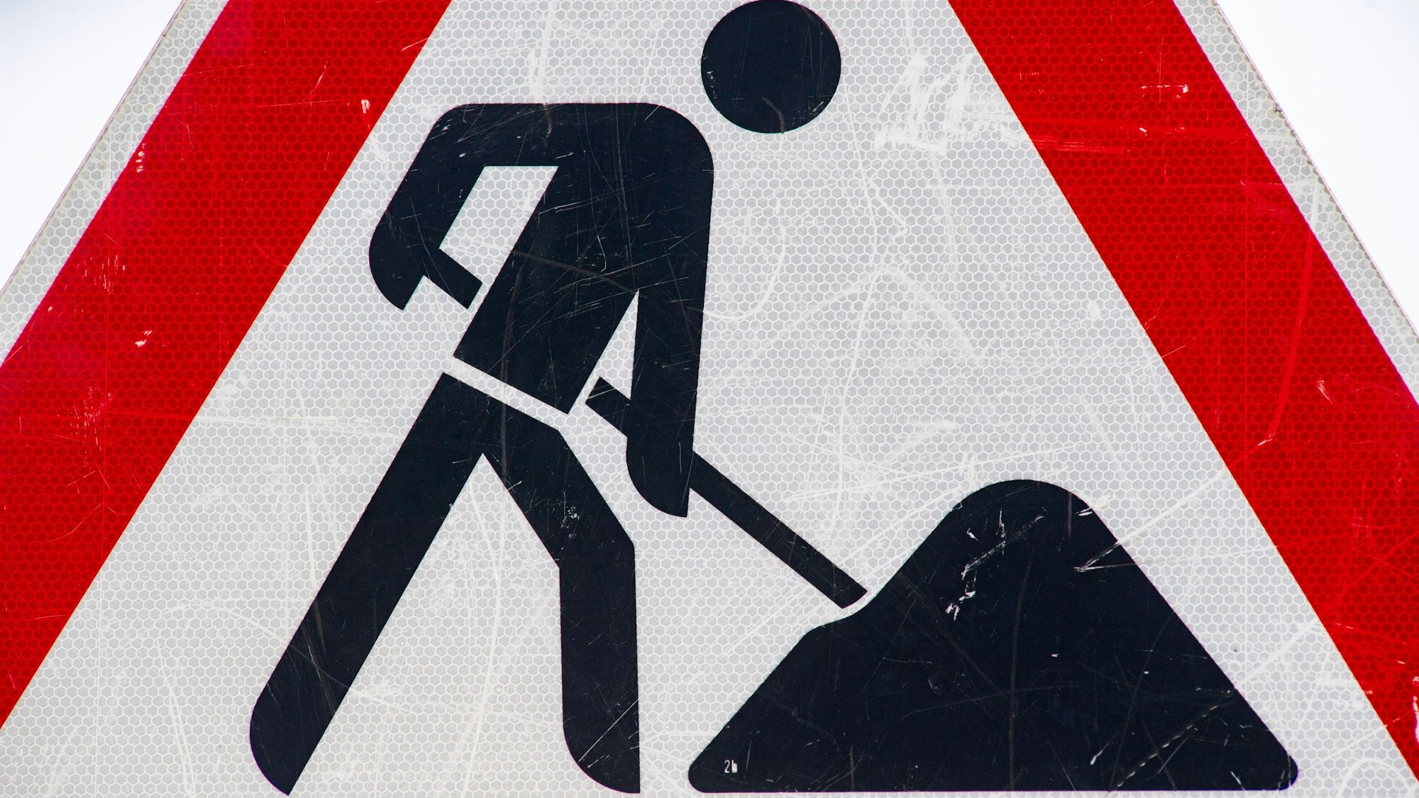 Zu sehen ist ein zerkratztes Schild mit dem Piktogramm eines Bauarbeiters zur Beschilderung einer Baustelle.