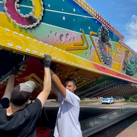 Zu sehen sind zwei Schausteller, die den Autoscooter aufbauen.