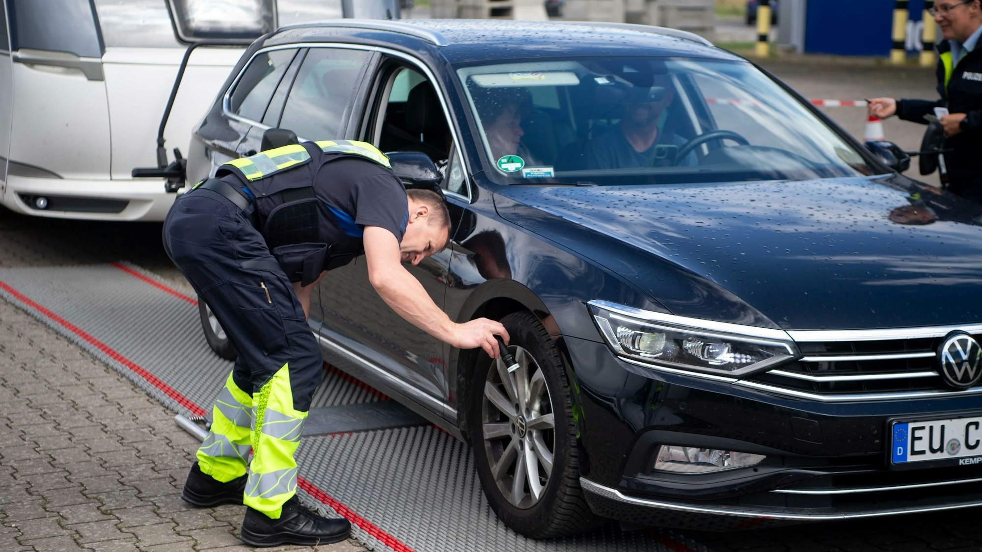 Ein Polizist leuchtet mit einer Taschenlampe an den Reifen eines Autos, dass auf eine Wage gefahren ist.