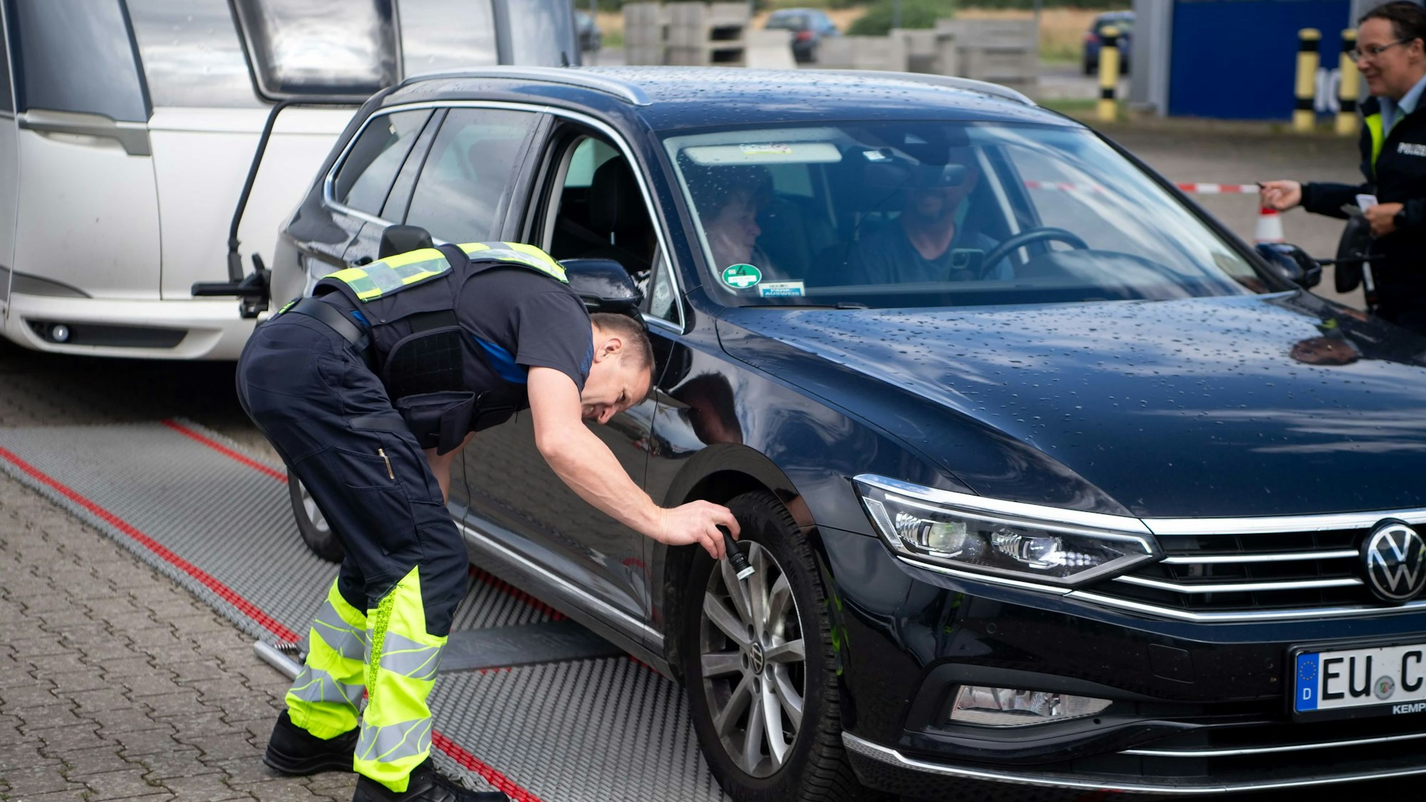 Ein Polizeibeamter leuchtet mit einer Taschenlampe in Richtung der Vorderbremsen eines Autos.