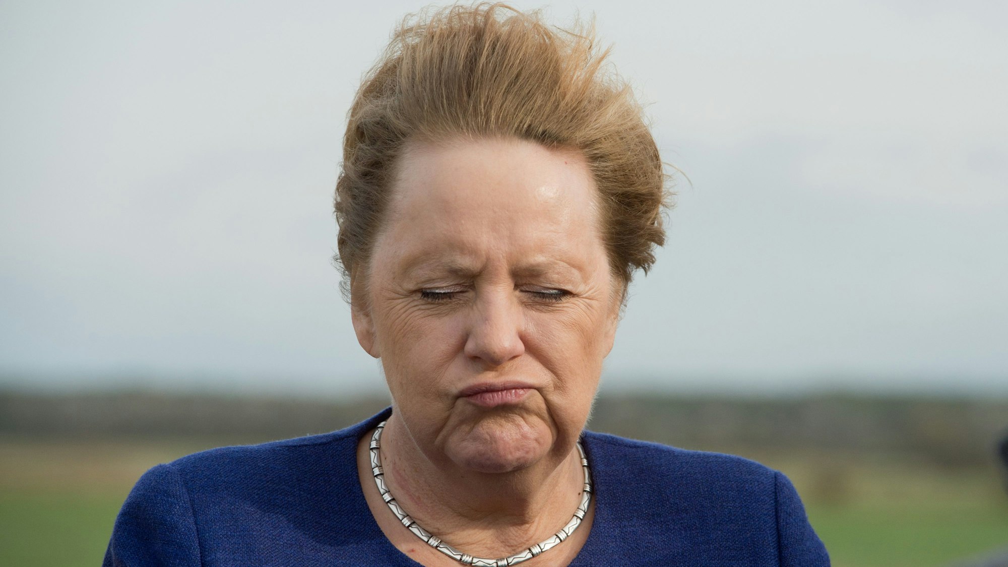 Angela Merkel steht mit vom Wind verwehten Haar auf einem Deich der Insel Ummanz.