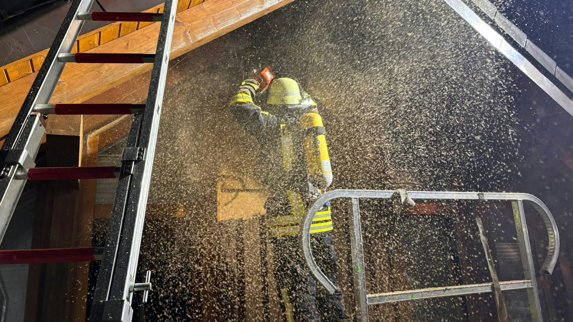 Ein Feuerwehrmann arbeitet unter Atemschutz an einem Haus in Blankenheim-Mülheim. Mit einer Motorsäge öffnet er die hölzerne Fassade.