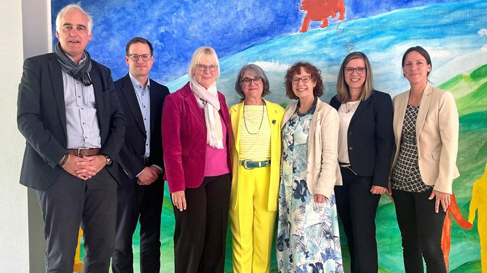 Männer und Frauen stehen vor einem großen Wandbild und lächeln.