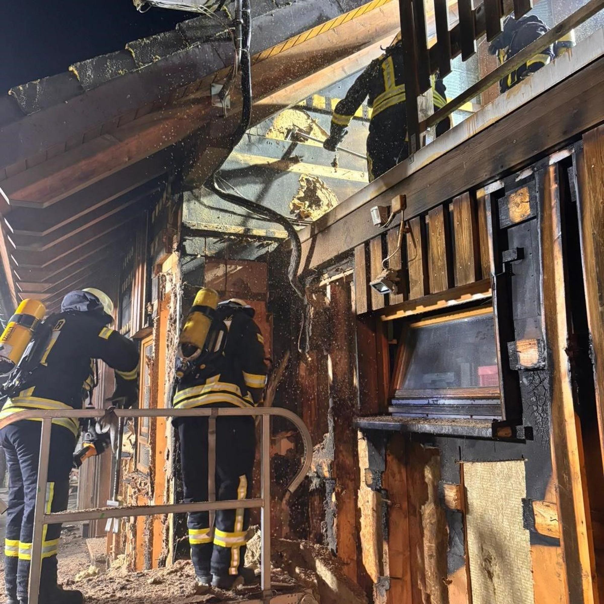 Feuerwehrleute arbeiten unter Atemschutz an einem Haus in Blankenheim-Mülheim. Sie haben die hölzerne Fassade geöffnet, zahlreiche schwarz verkohlte Stellen sind zu erkennen.